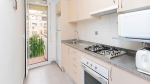 Eine kleine Küche mit Gasherd, Backofen und Toaster. Eine Glastür führt zu einem Balkon mit Blick auf Gebäude.
