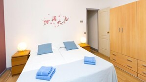 Ein Schlafzimmer mit einem Doppelbett, zwei Nachttischen mit Lampen, einem Kleiderschrank und einer Wanddekoration mit floralem Muster.
