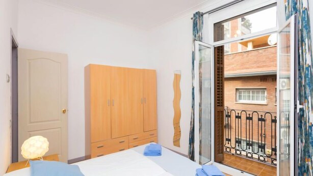 Ein Schlafzimmer mit Bett, Kleiderschrank und einem Balkon mit Blick auf ein Backsteingebäude.