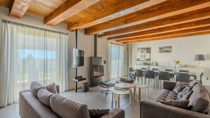 A spacious living area with a high wooden ceiling, a television, a fireplace, and a dining area with chairs and a table. - Modern villa with heated pool and Jacuzzi, near Ripe, just 20 minutes from the beach of Senigallia (Trecastelli)