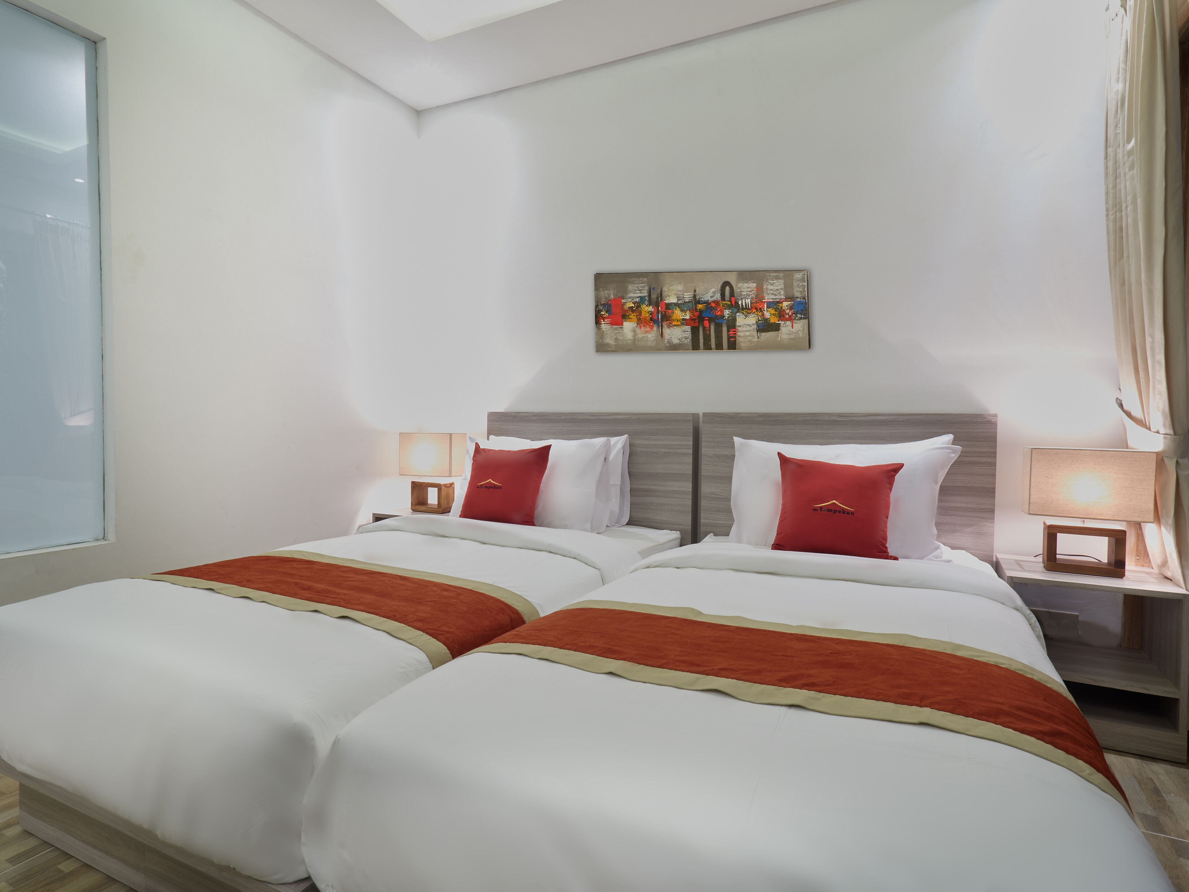 A hotel room with two beds, a painting on the wall, and a window.