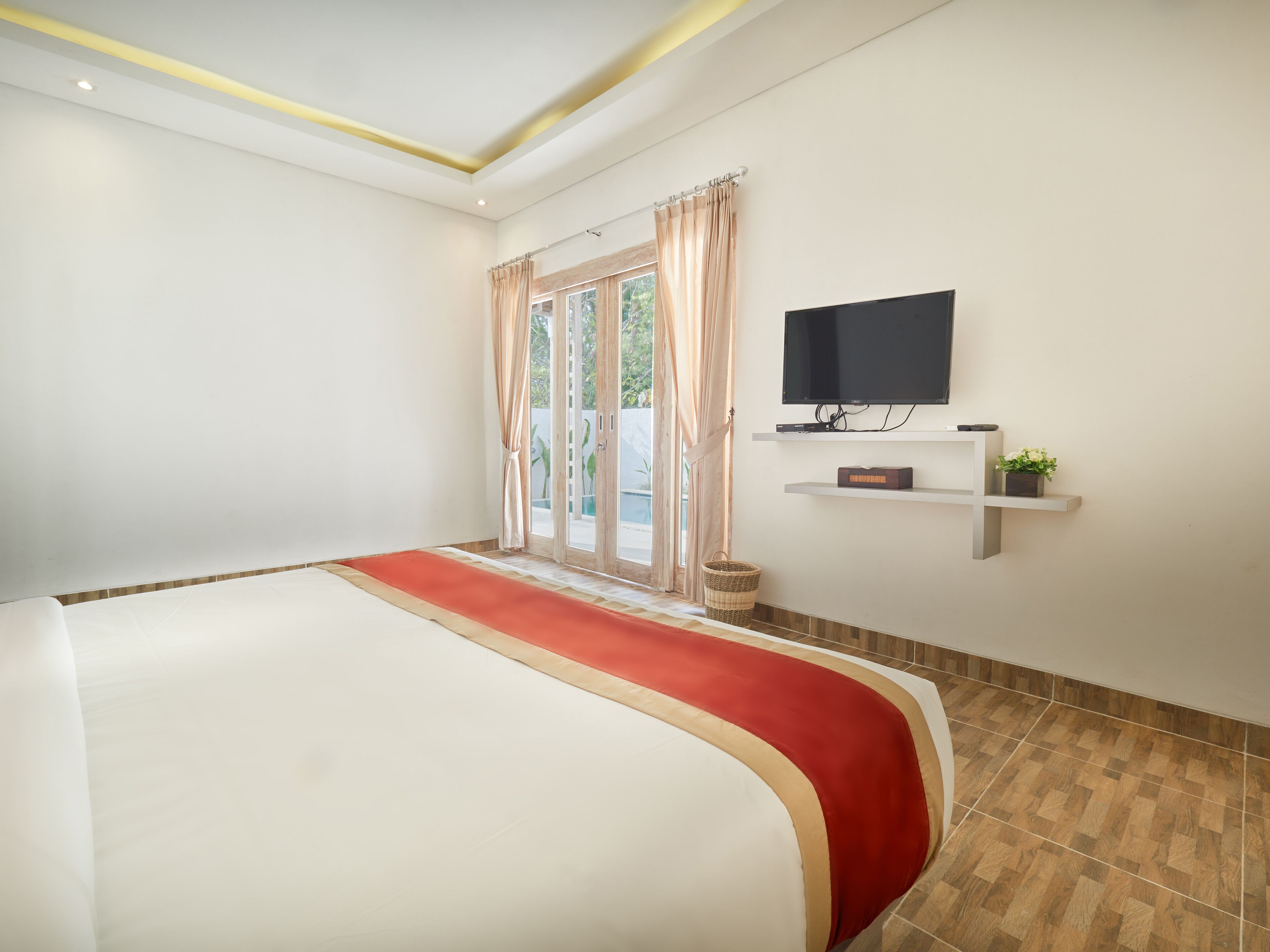 A hotel room with a large bed, a television mounted on the wall, and a small shelf with a plant.