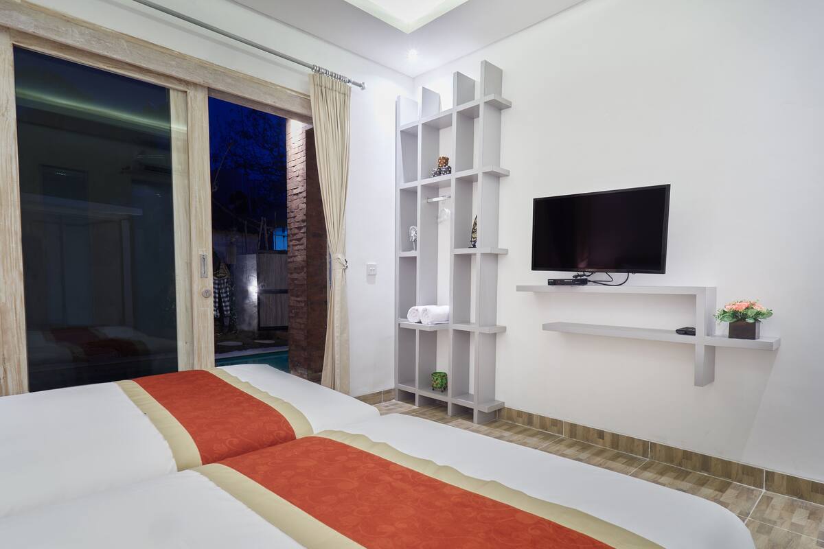 A hotel room with two beds, a TV, a shelf with toiletries, and a view of the outside.
