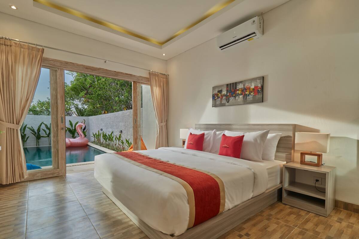 A spacious bedroom with a large bed, a nightstand, and a view of a swimming pool.