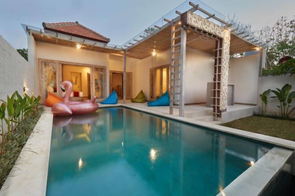 A swimming pool with inflatable toys, a covered patio, and a house with a tiled roof.
