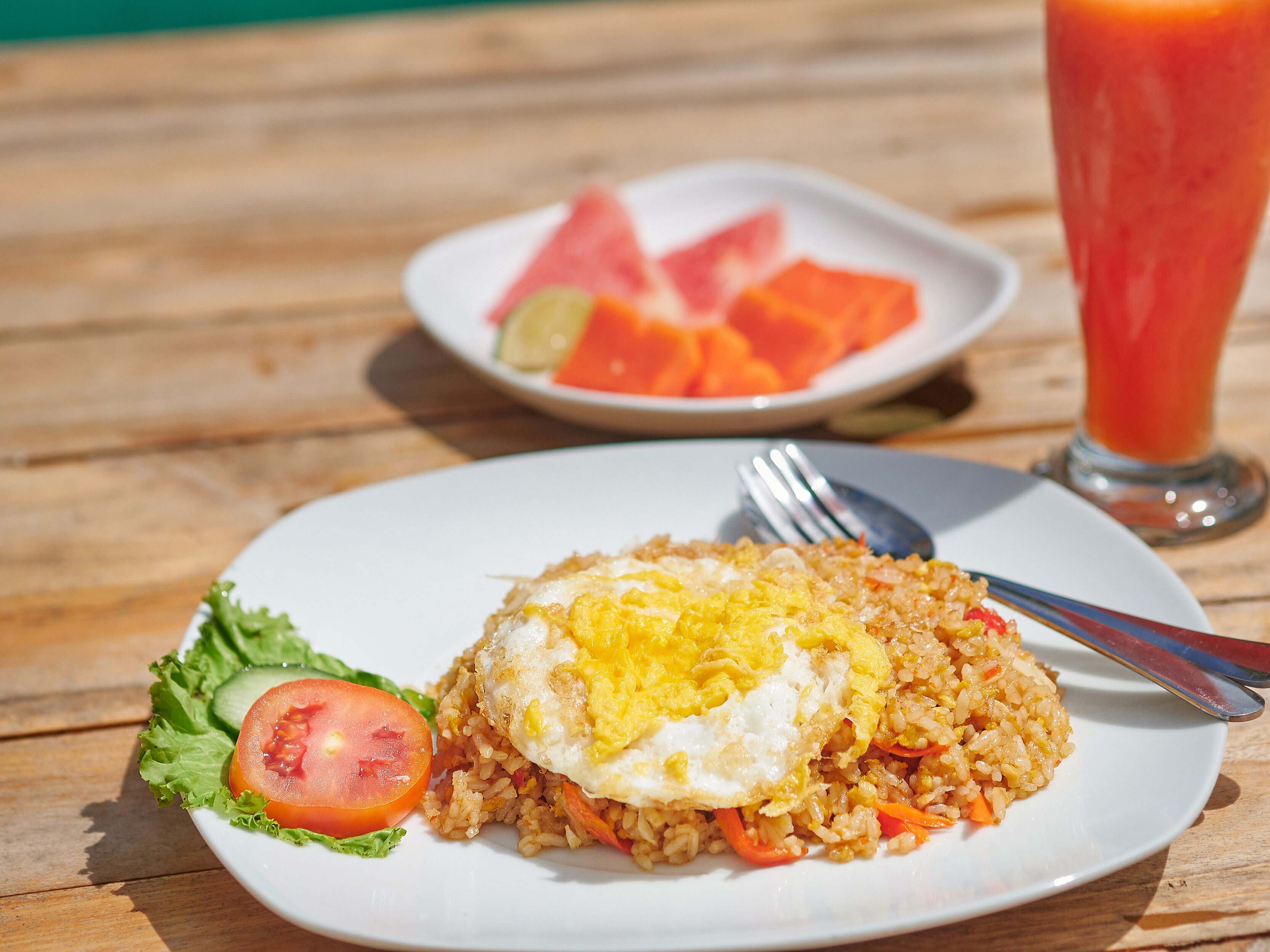 A plate of fried rice with an egg, a slice of tomato, and lettuce on a wooden table.
