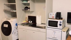 A compact kitchen with a washing machine, a microwave, and a small refrigerator. - Amami Lucky Life (Amami)