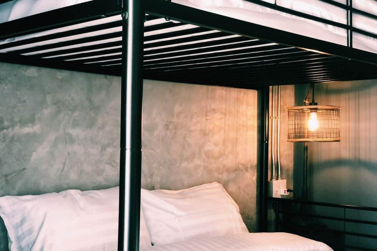 Ein Stockbett mit weißer Bettwäsche, einem Metallgestell und einer Wandleuchte.