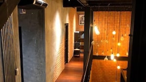 A narrow hallway with a staircase leading to a lower level. The walls are made of exposed brick, and there are hanging light fixtures. - The LOCAL Ari - Hostel (Bangkok)