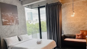 A modern bedroom with a large bed, a sofa, a view of the city, and a curtain. - The LOCAL Ari - Hostel (Bangkok)