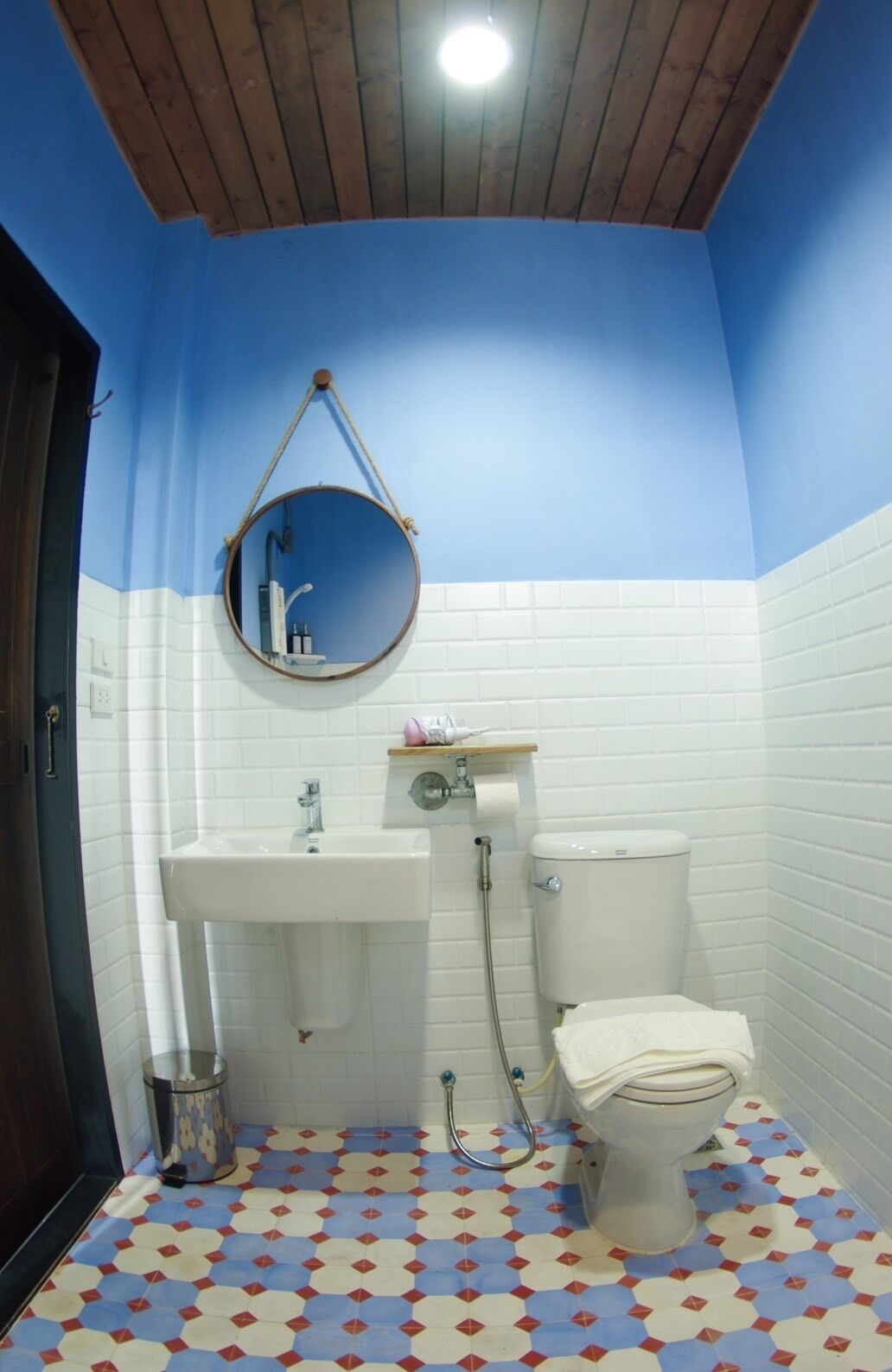 A bathroom with a white sink, toilet, and a round mirror hanging from the ceiling.