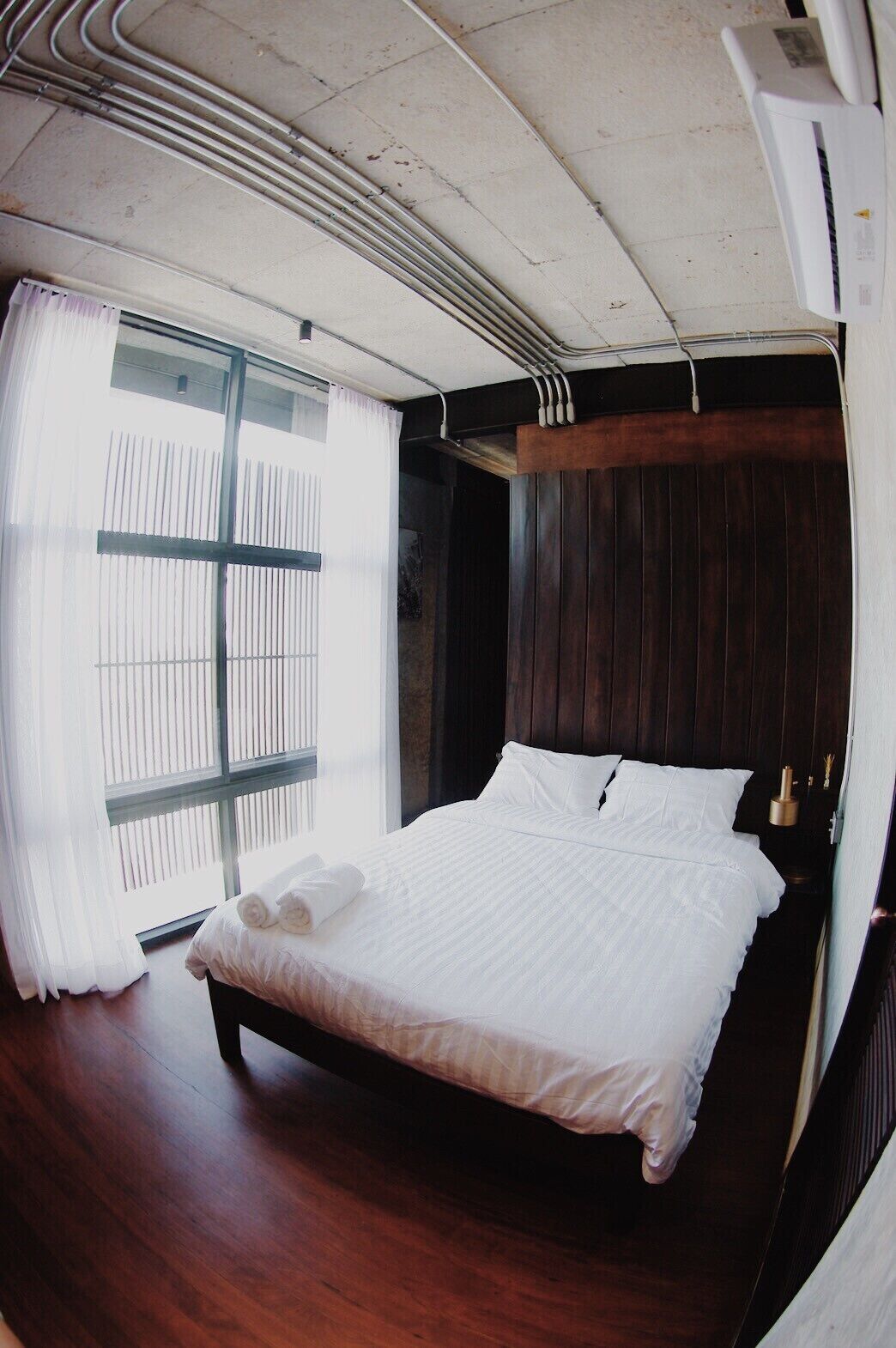 Un dormitorio moderno con una cama grande, suelo de madera, una ventana con persianas y un equipo de aire acondicionado.