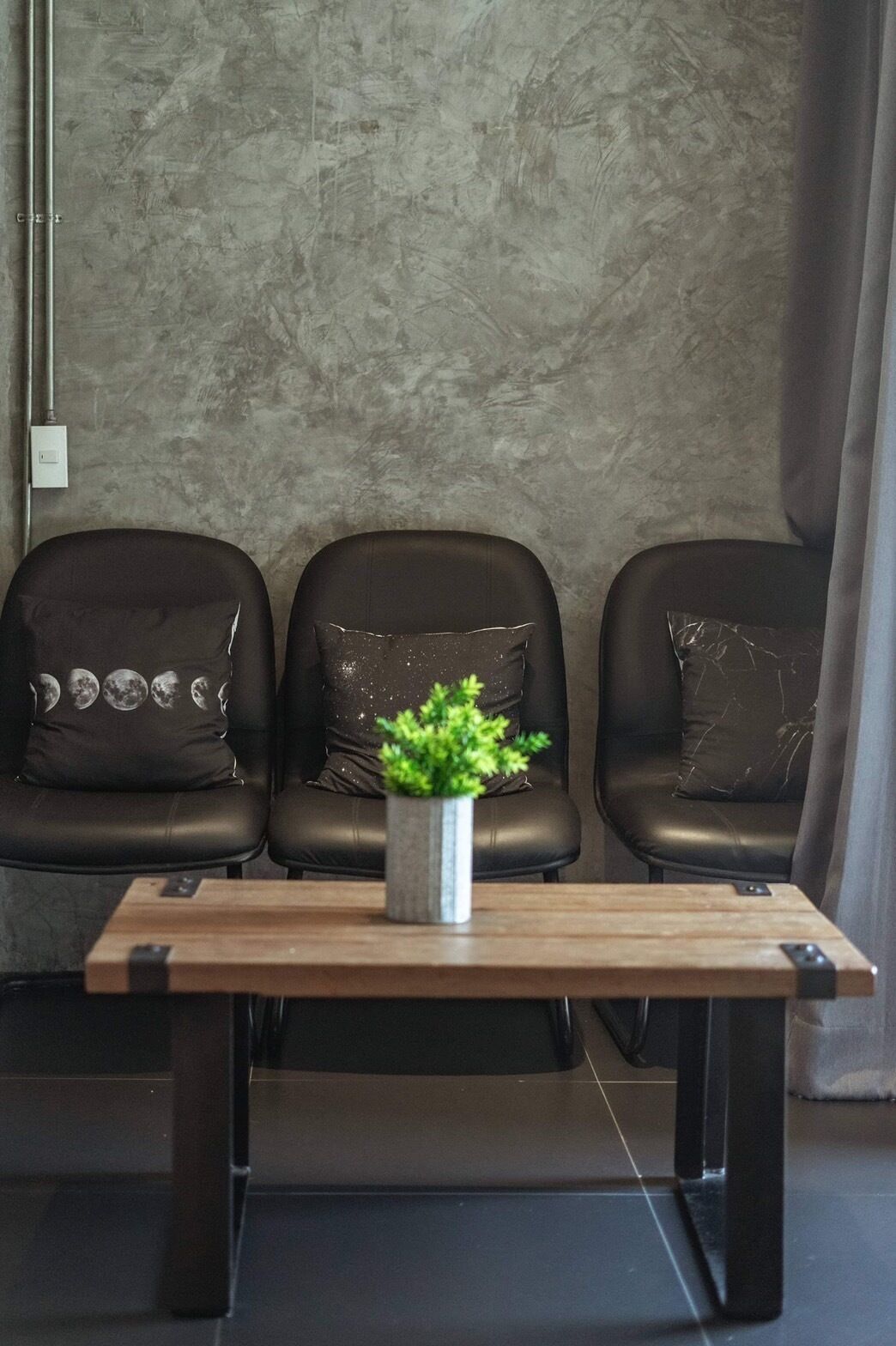 A seating area with three black leather chairs, each with a unique pillow design. A small metal table with a plant is in front of the chairs.