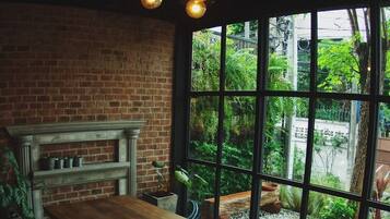A rustic dining area with a wooden table and bench, brick walls, and large windows overlooking a garden.
