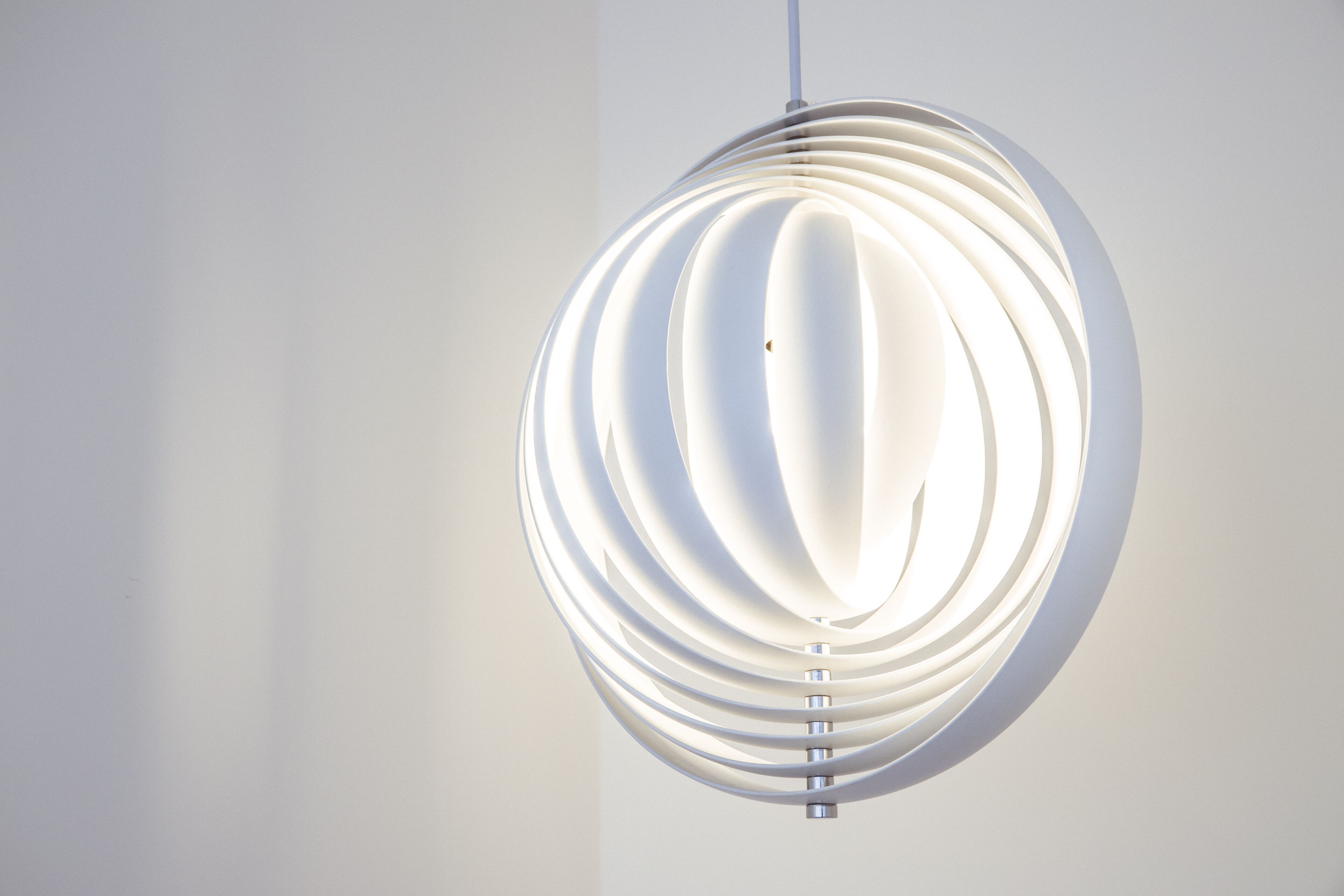 A modern, spherical pendant light fixture with a white, ribbed design against a plain wall.