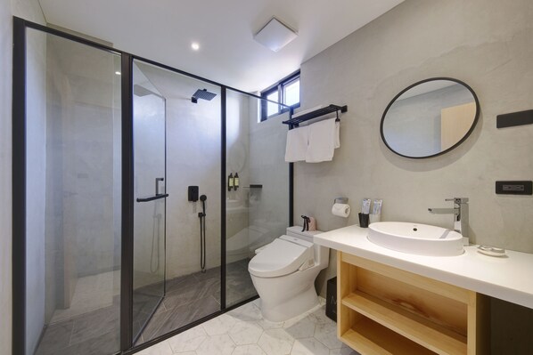 Un baño moderno con ducha de vidrio, inodoro blanco, lavamanos con espejo y toallero.