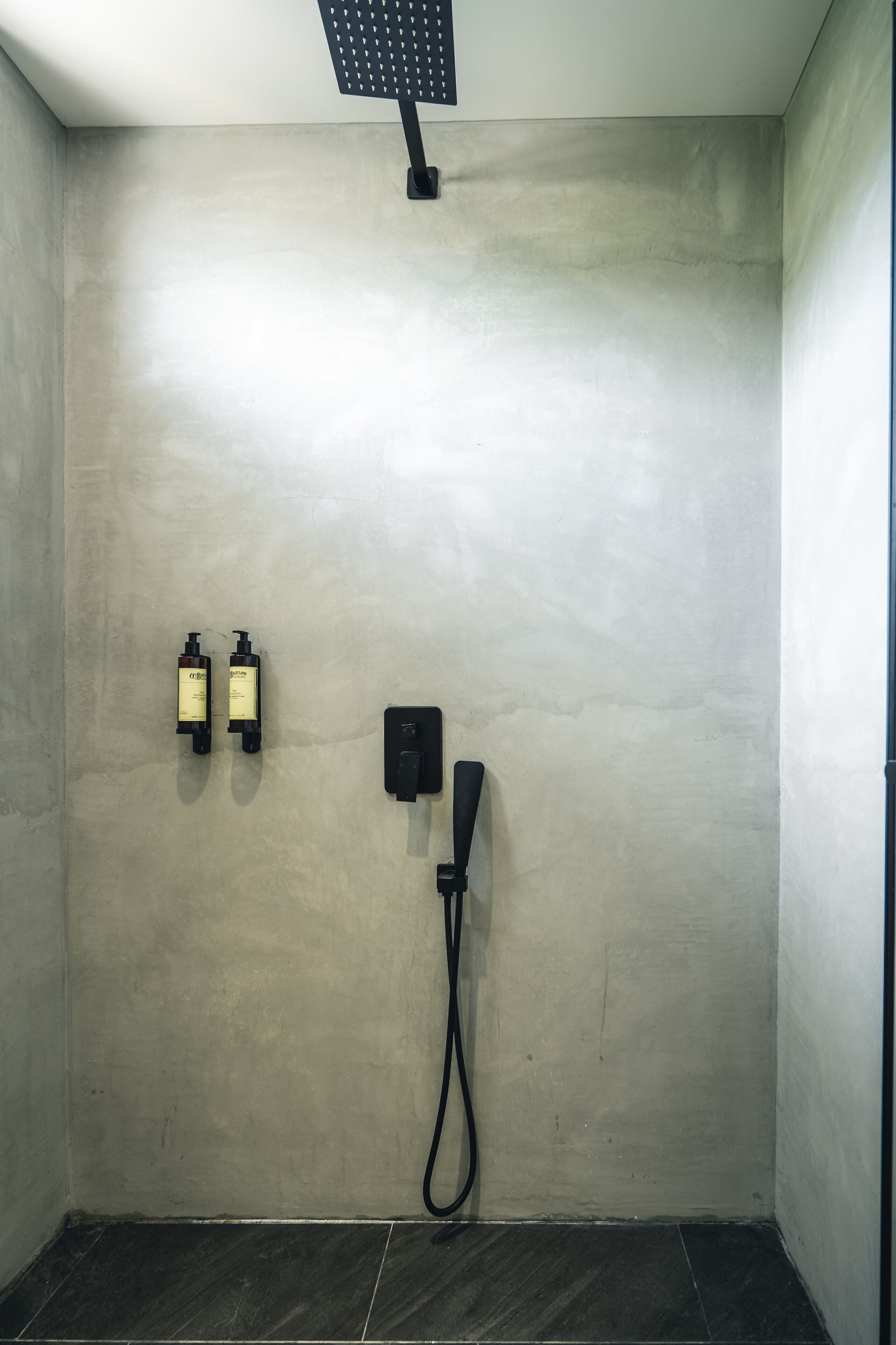 A shower area with a wall-mounted faucet and two bottles of shampoo.