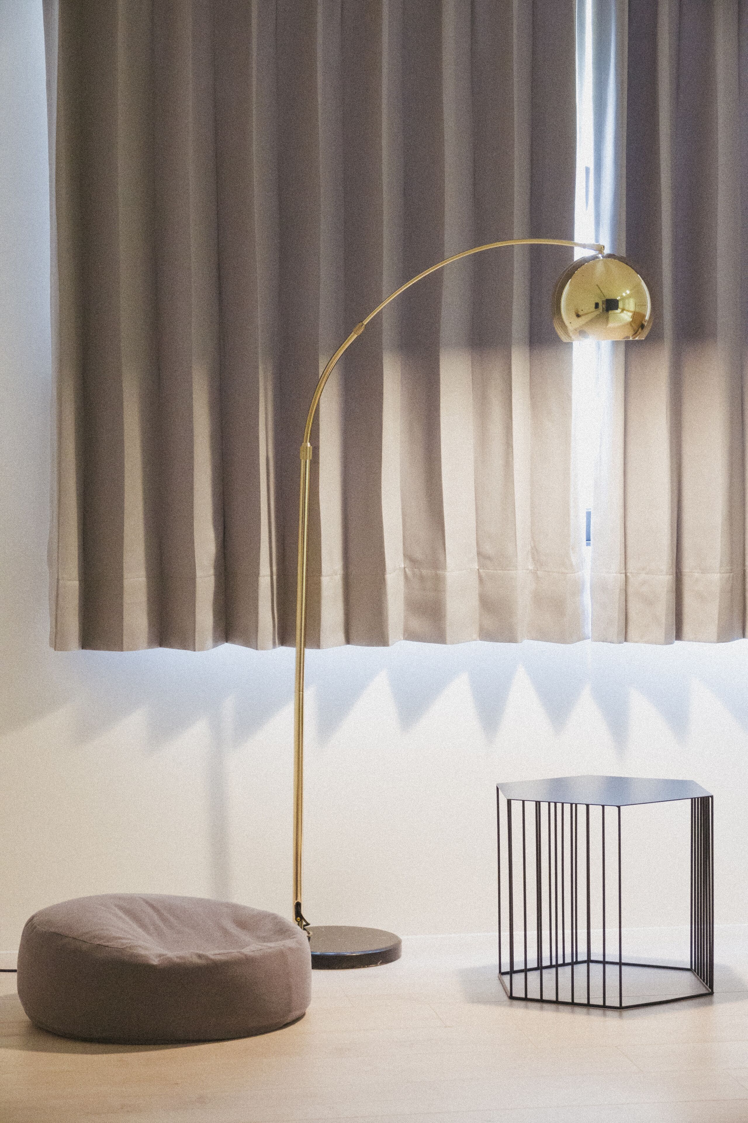 A room with a floor lamp, a round ottoman, and a geometric side table.