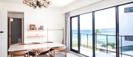 Un dormitorio moderno con una cama grande, una mesa de comedor con sillas y vistas al océano a través de amplios ventanales.