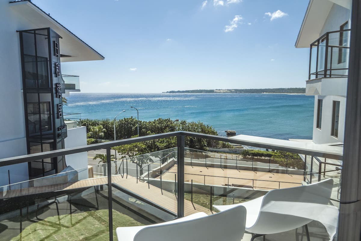 Un balcón con vistas al mar, sillas blancas y una fachada de edificio moderna.