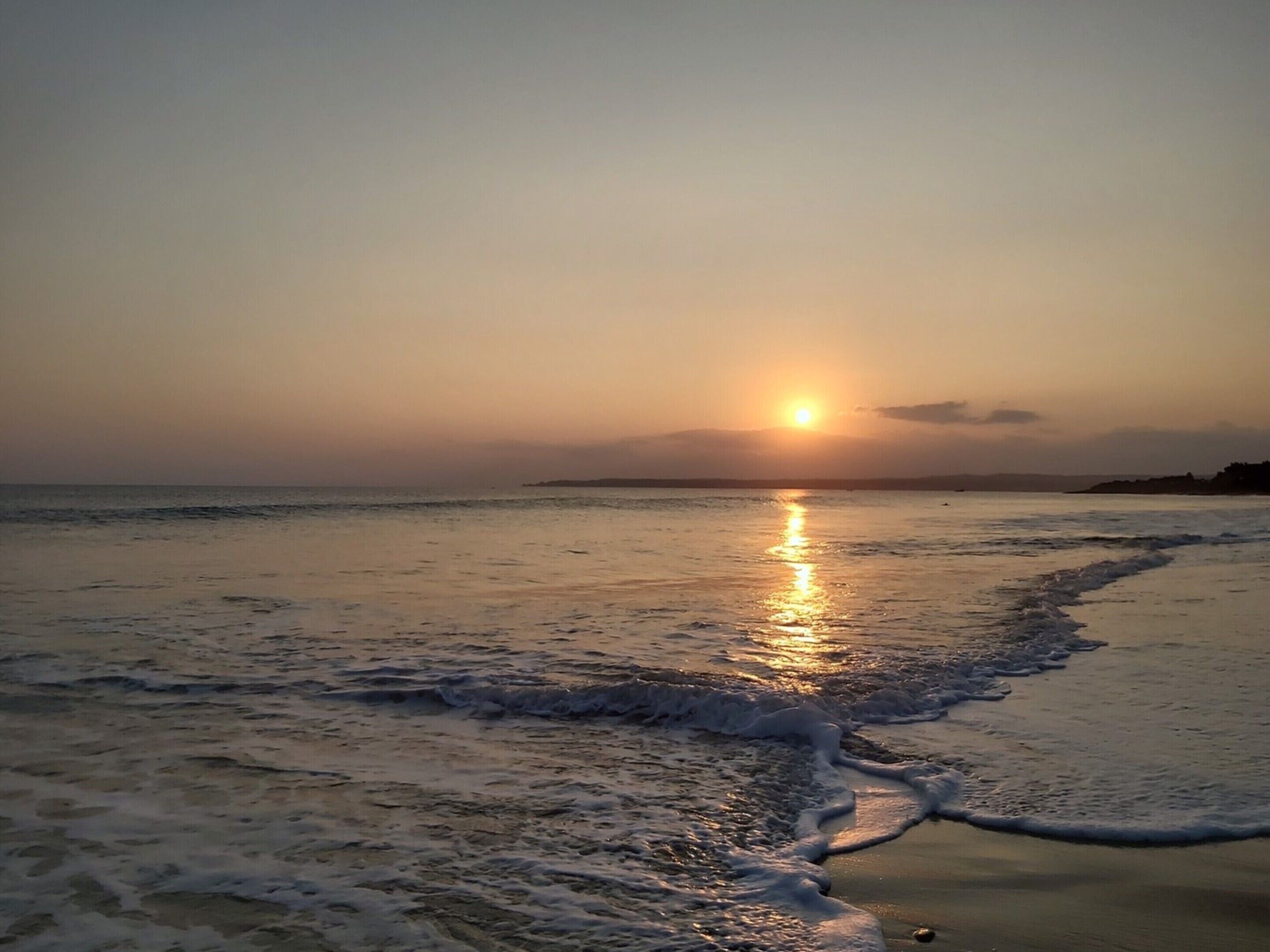A beach at sunset with waves gently lapping the shore.