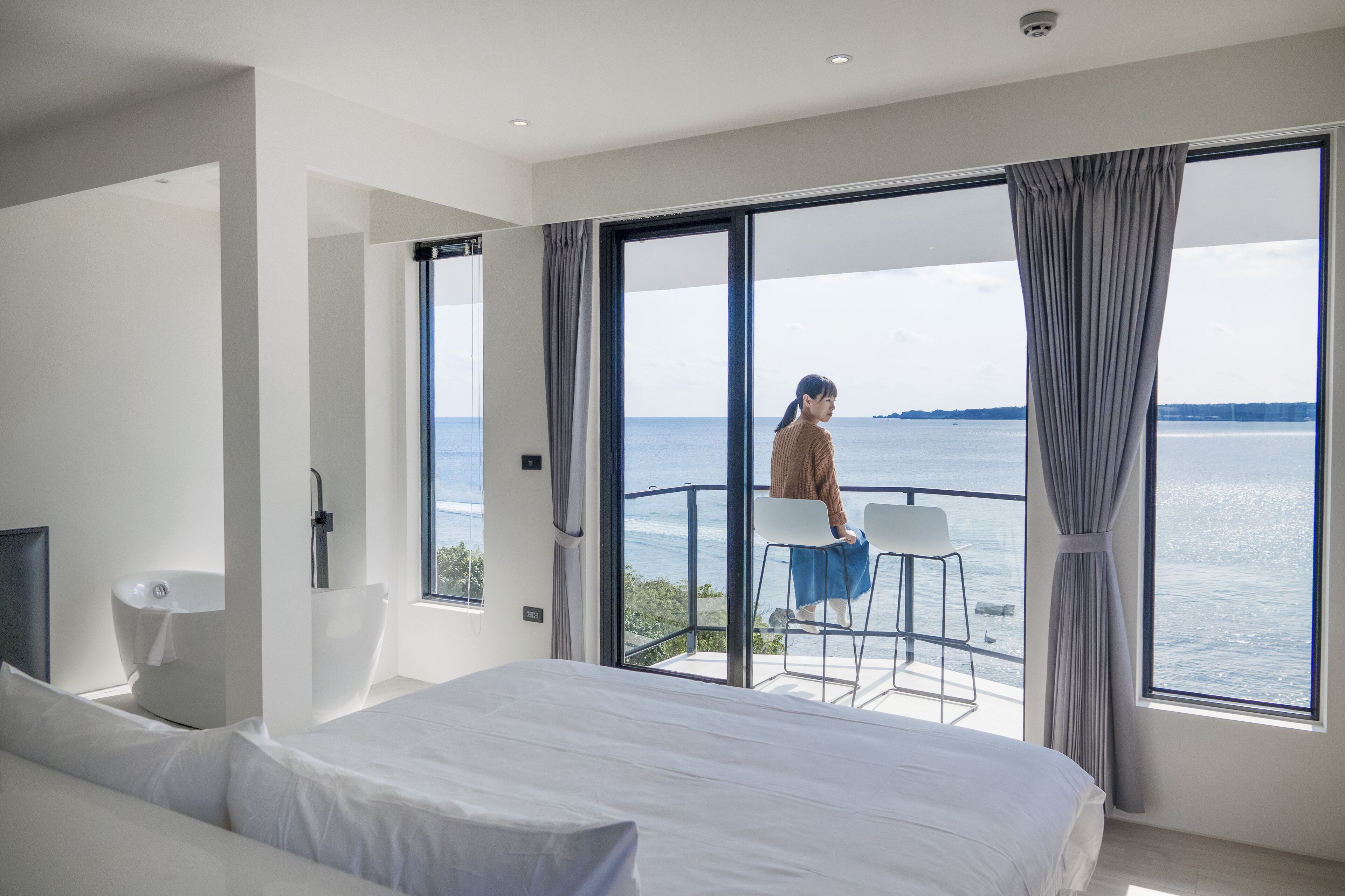 Una habitación de hotel moderna con una cama grande, una bañera y un balcón con vistas al mar.