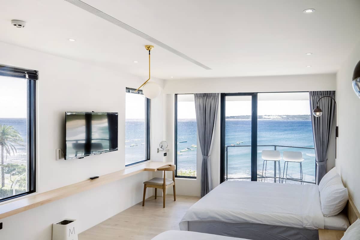 Un dormitorio moderno con una cama grande, un escritorio y un televisor. Cuenta con un balcón con vistas al mar.