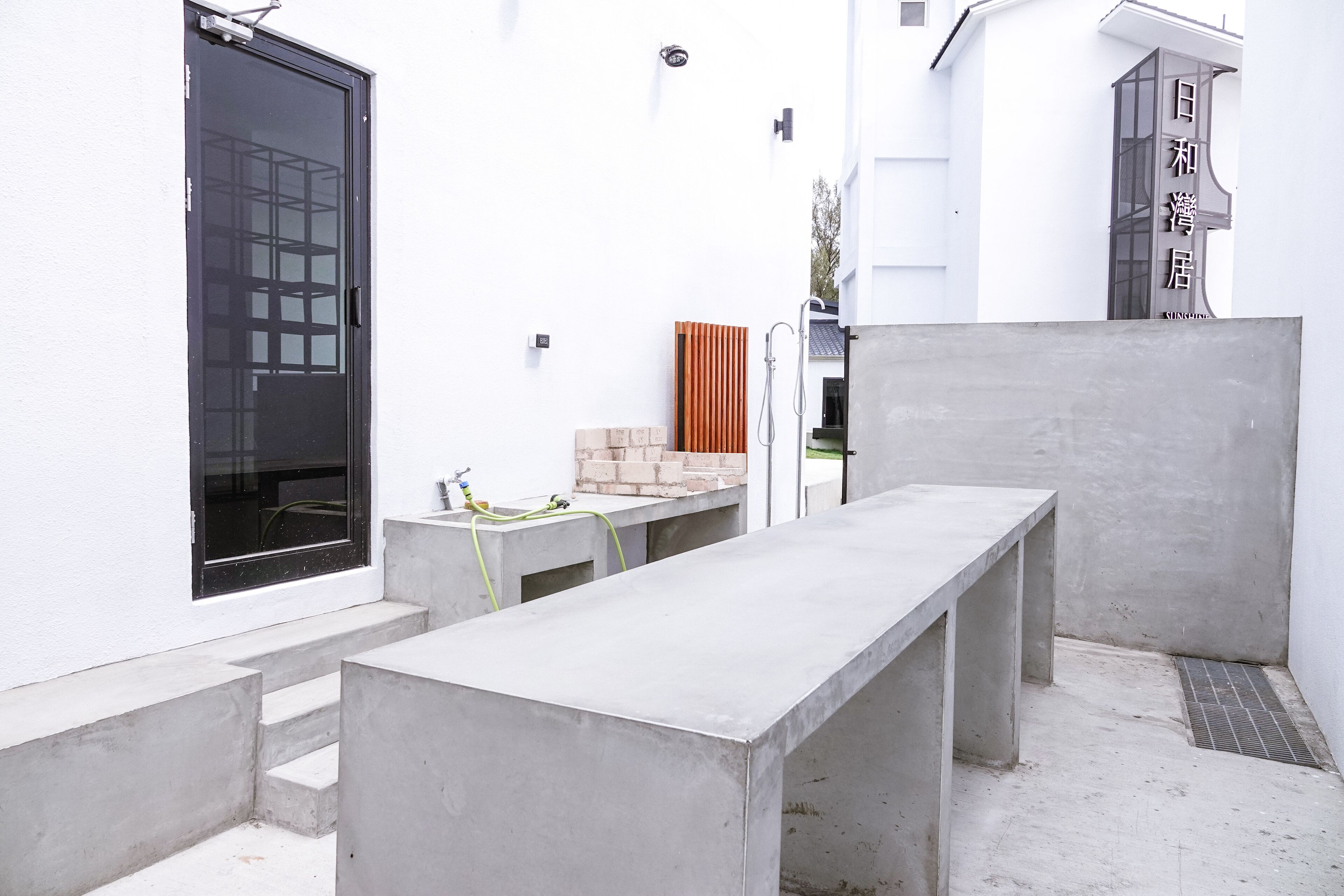 A modern outdoor area with concrete benches, a black door, and a white building with a sign in a foreign language.
