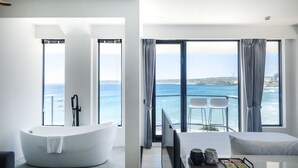 Une chambre d’hôtel moderne dotée d’une grande baignoire, d’un lit, d’une télévision et d’un coin repas offrant une vue sur la mer.