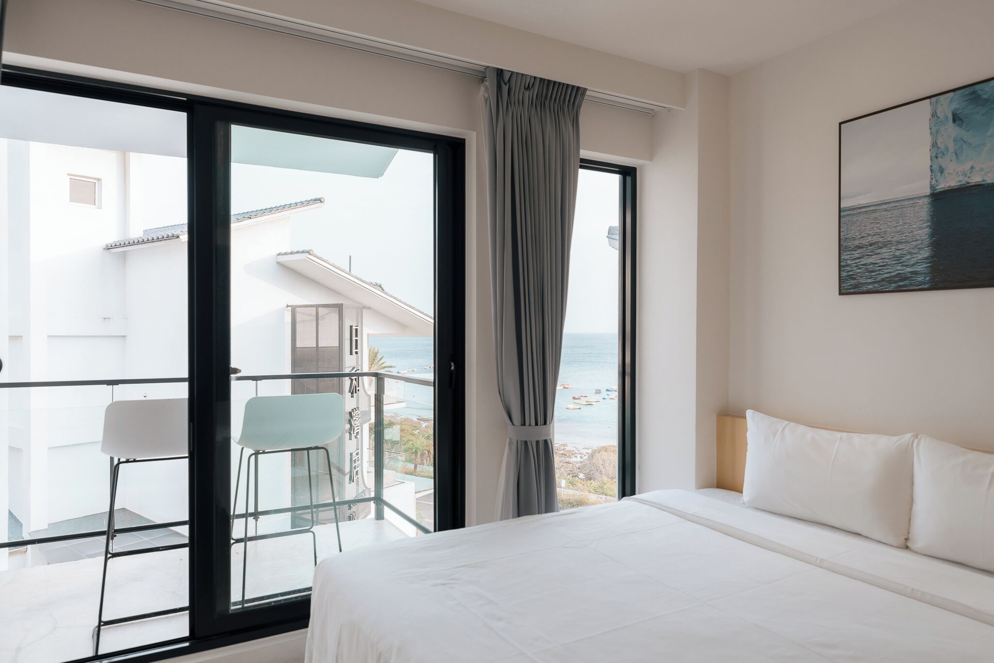 A hotel room with a large bed, a balcony with a view of the sea, and a chair.