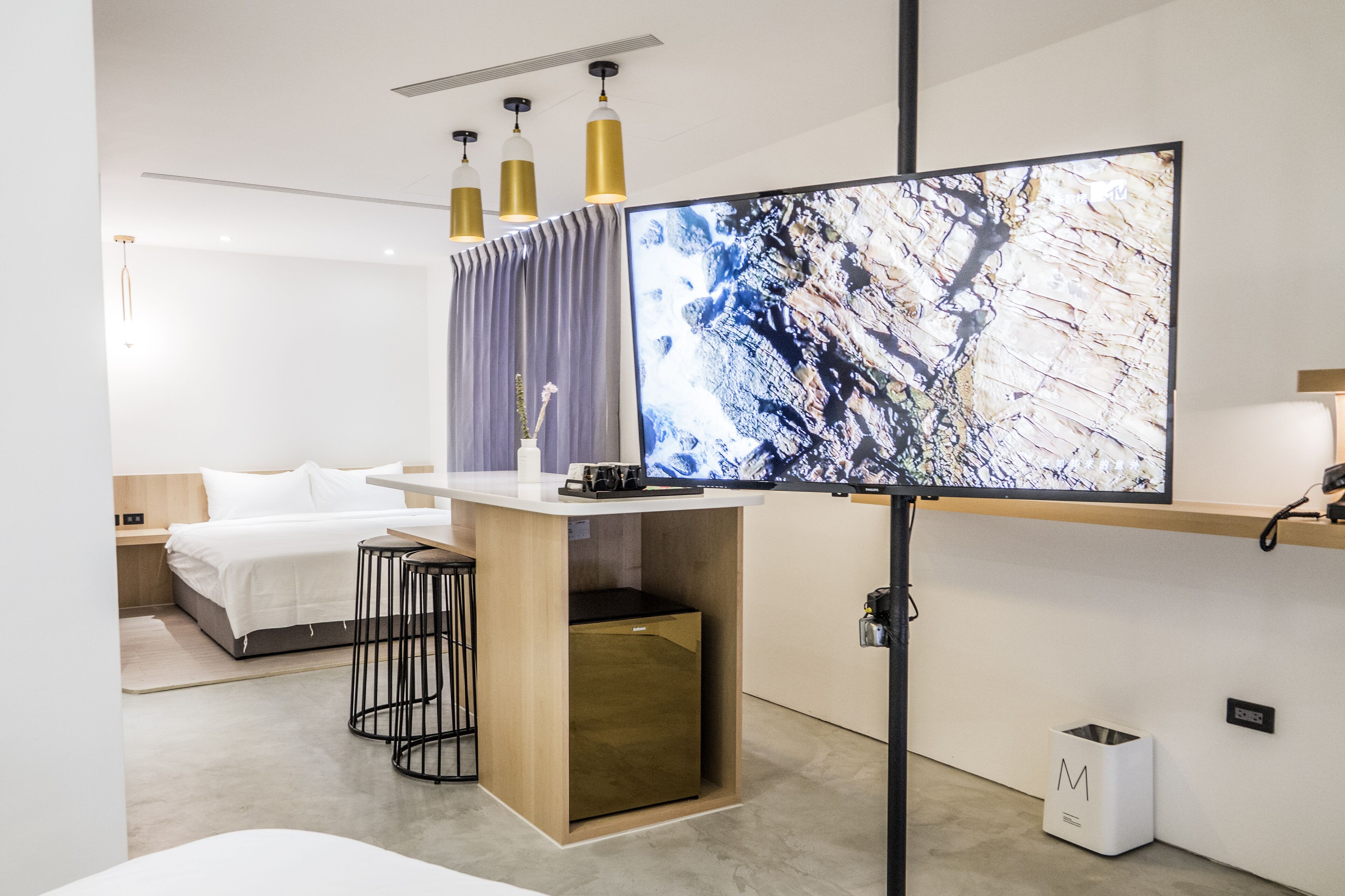 Et moderne hotelværelse med stort fladskærms-tv, seng med hvide sengetøj, et lille skrivebord med stol og et træskab.