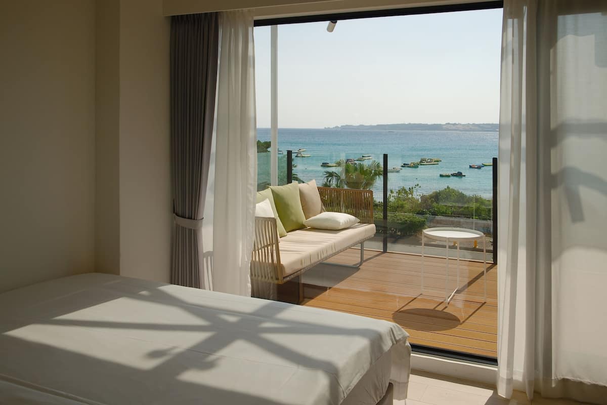 Un dormitorio con una cama grande, un balcón con sofá y una mesita, y vista al mar.