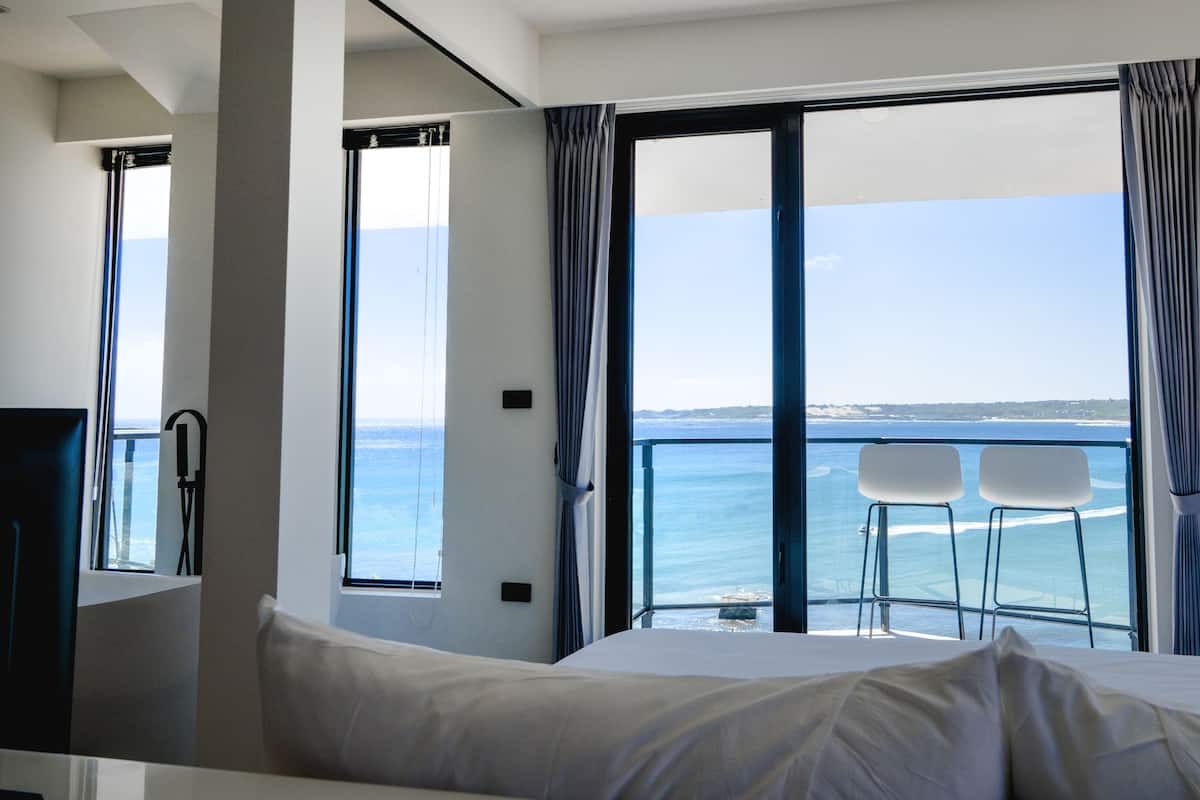 Una habitación de hotel con cama, ventana con cortinas y vista al mar.