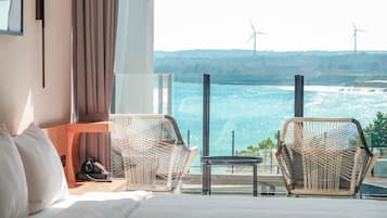 Habitación de hotel con cama, dos sillones de mimbre, una mesita y vistas al mar y a aerogeneradores.