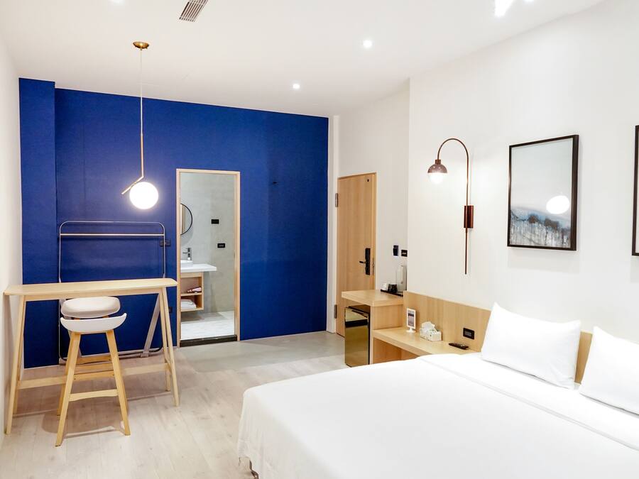 A modern hotel room with a bed, a desk, and a bathroom.