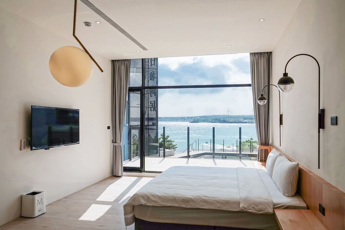 Un dormitorio moderno con una cama grande, un televisor y vista al mar.