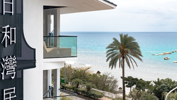 Un bâtiment moderne doté d’un balcon donnant sur une plage où sont amarrés des bateaux.