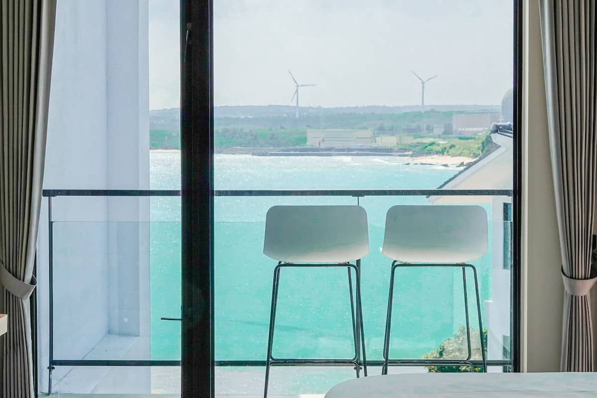 Vista desde un balcón con dos sillas, con vista a un cuerpo de agua y aerogeneradores a lo lejos.
