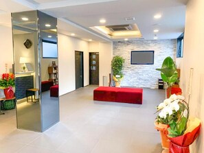 A modern interior with a red sofa, a flat-screen TV, and a stone wall. - Hotel Livemax Okayama West (Okayama)