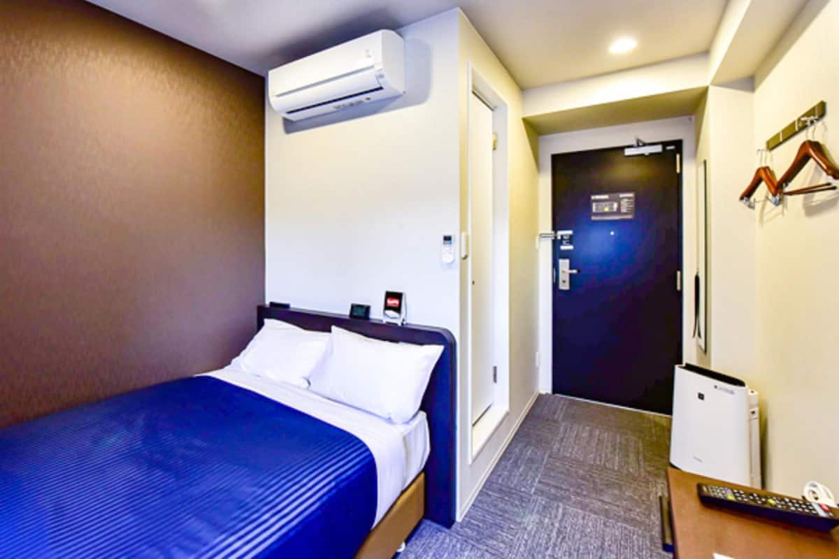 Habitación de hotel con cama, aire acondicionado, escritorio con control remoto y puerta que da a otra habitación.