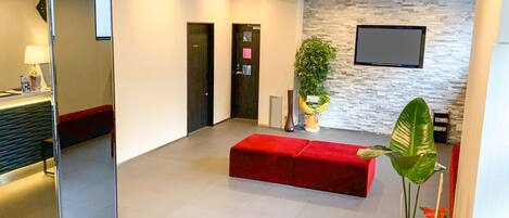 Ein moderner Empfangsbereich mit einem roten Sofa, einem Empfangstresen, einem wandmontierten Fernseher und einer großen Topfpflanze.