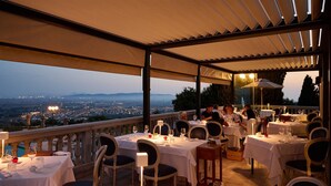 An outdoor dining area with tables set for dinner, overlooking a cityscape at dusk. - Castello Bonaria Wine & Spa Resort (Campiglia Marittima)