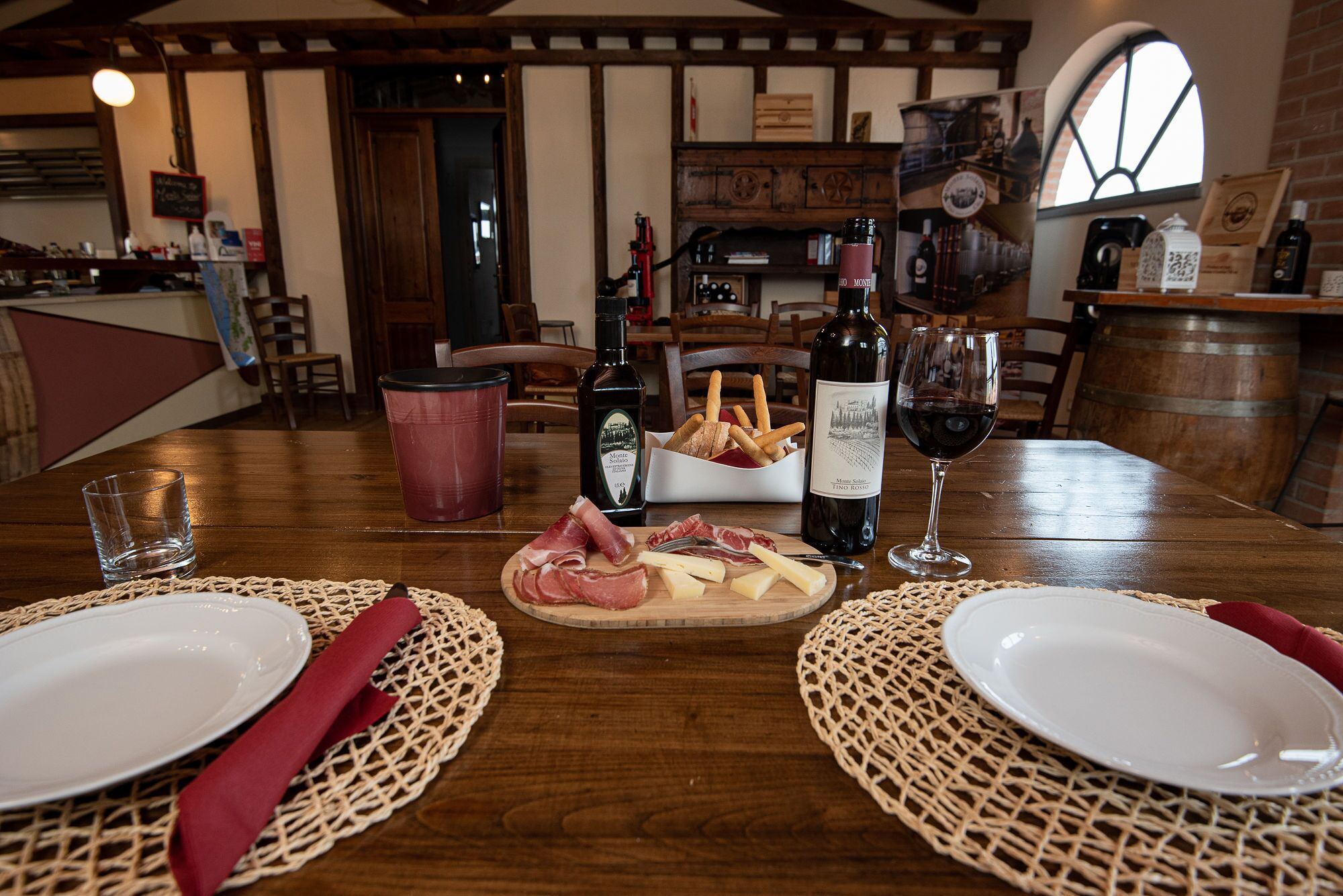 A wooden dining table set with plates, cutlery, a bottle of wine, and a basket of breadsticks.