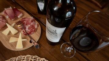 Una mesa de madera con una botella de vino, una copa de vino tinto, queso y embutidos.