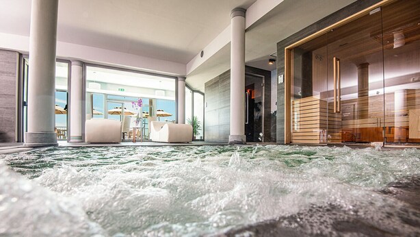 A spa area with a hot tub surrounded by columns and a seating area with umbrellas. - Castello Bonaria Wine & Spa Resort (Campiglia Marittima)