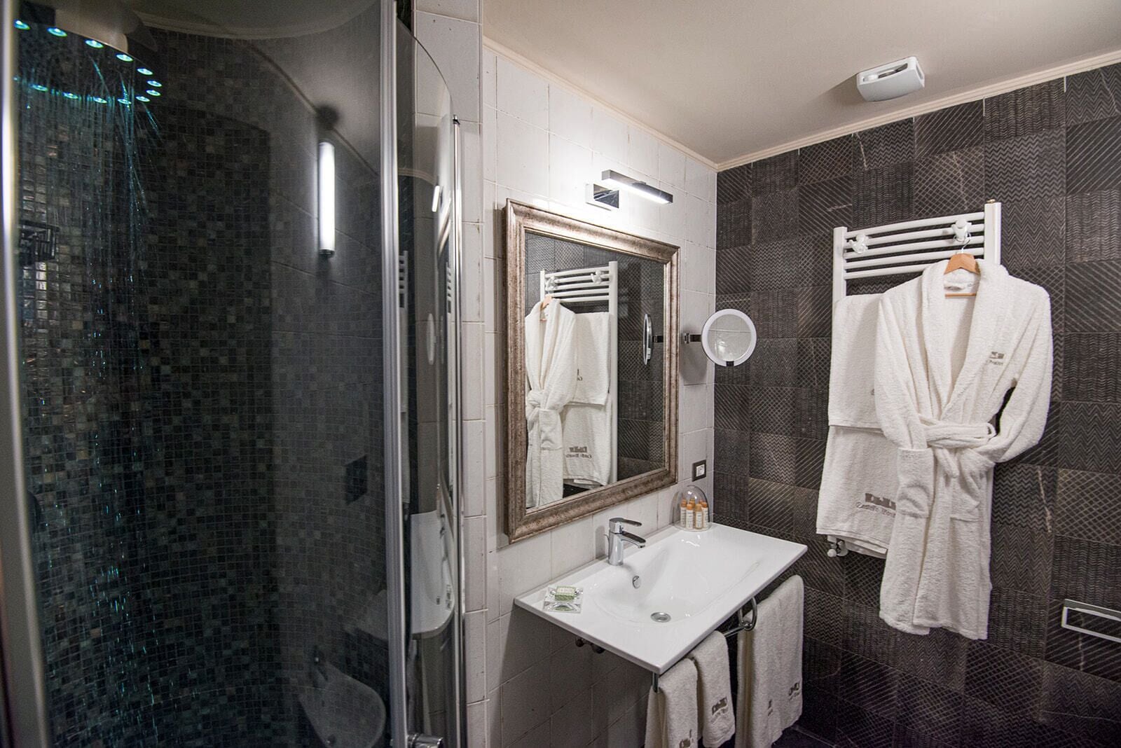 Un bany modern amb dutxa de vidre, un lavabo blanc i un mirall gran.