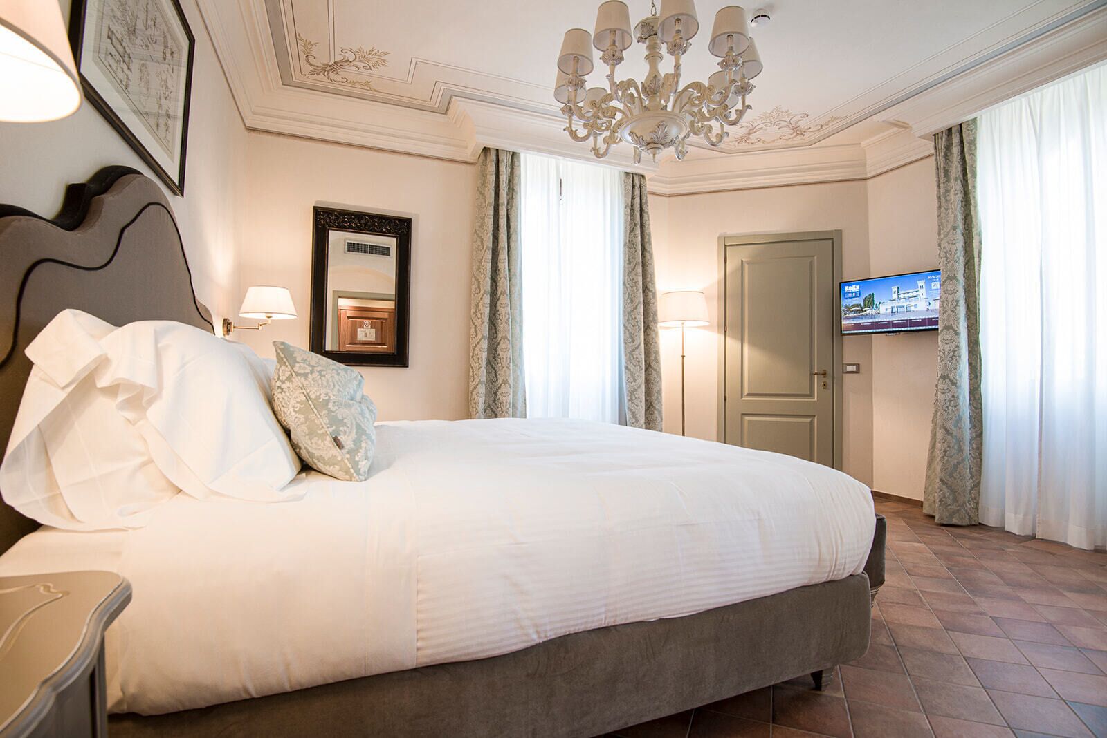 A hotel room with a large bed, a chandelier, a television, and a door.
