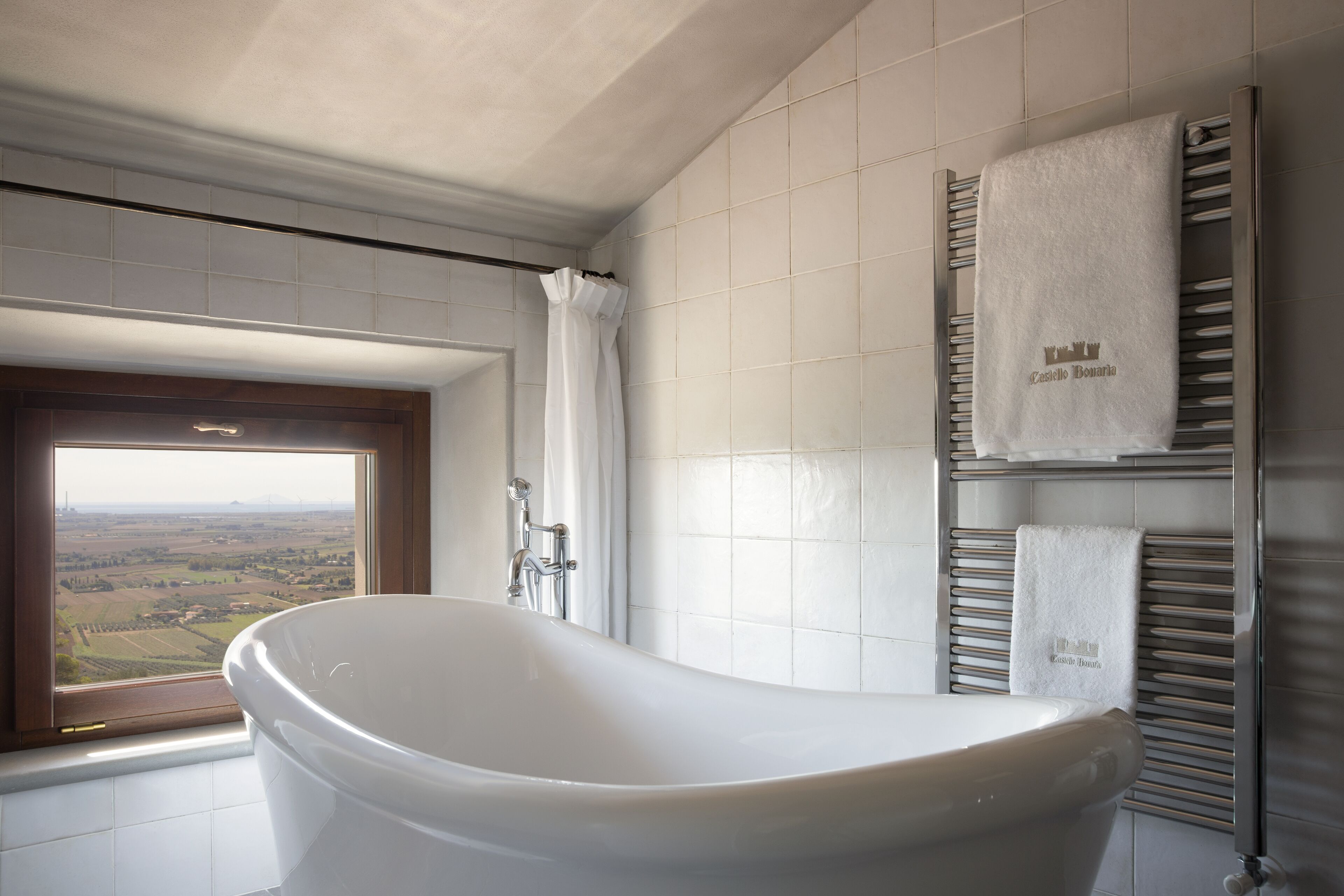 Une salle de bain moderne avec une baignoire sur pieds, une fenêtre donnant sur la campagne et un porte-serviettes avec des serviettes de marque.