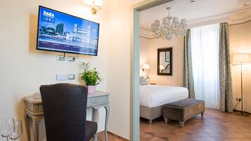 Una camera d'hotel con un letto, una scrivania con una sedia, una TV a parete e una pianta in vaso.