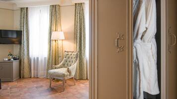 Quarto de hotel com poltrona estofada, mesa de cabeceira com abajur e guarda-roupa com roupões.